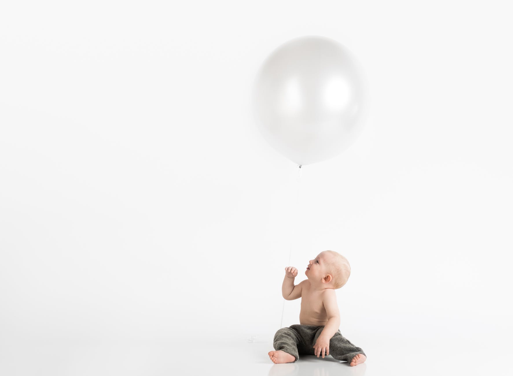 topless toddler with pants sitting on white surface while looking up