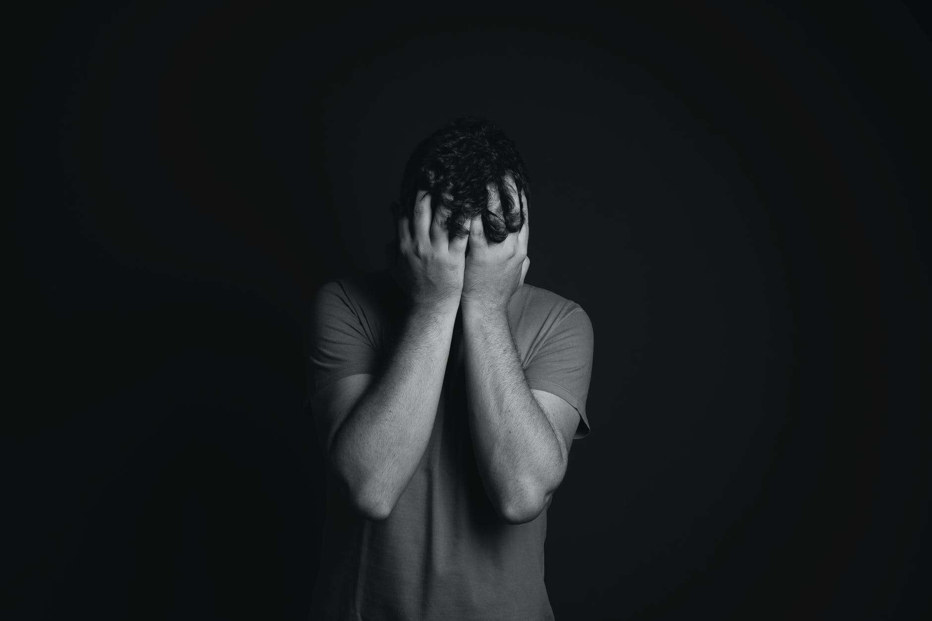 gray scale photo of man covering face with his hands